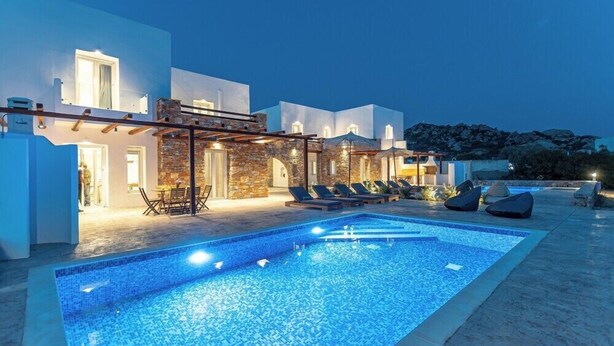 Un edificio moderno con piscina, mobiliario exterior y un muro de piedra.