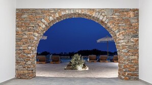Un área de estar al aire libre con muros de piedra, un pequeño árbol y sillones de descanso.