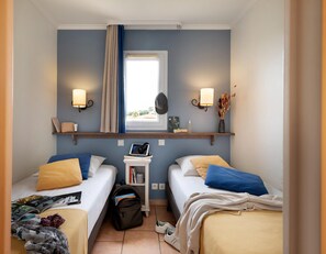 A hotel room with two beds, a window with curtains, wall-mounted lamps, a small table with books and a laptop, and a backpack on the floor. - Stunning 4-person Sea View Haven (Roquebrune-sur-Argens)