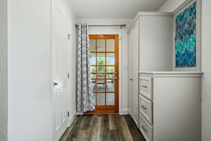 A hallway with a wooden door, a patterned curtain, a white cabinet, and a blue abstract painting. - Keep Me In Mind | Pool | Hot Tub | New Braunfels (New Braunfels)