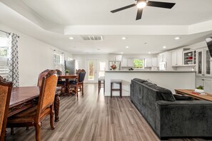 A modern kitchen with white cabinets, a dining area with a wooden table and chairs, and a grey sofa. - Keep Me In Mind | Pool | Hot Tub | New Braunfels (New Braunfels)