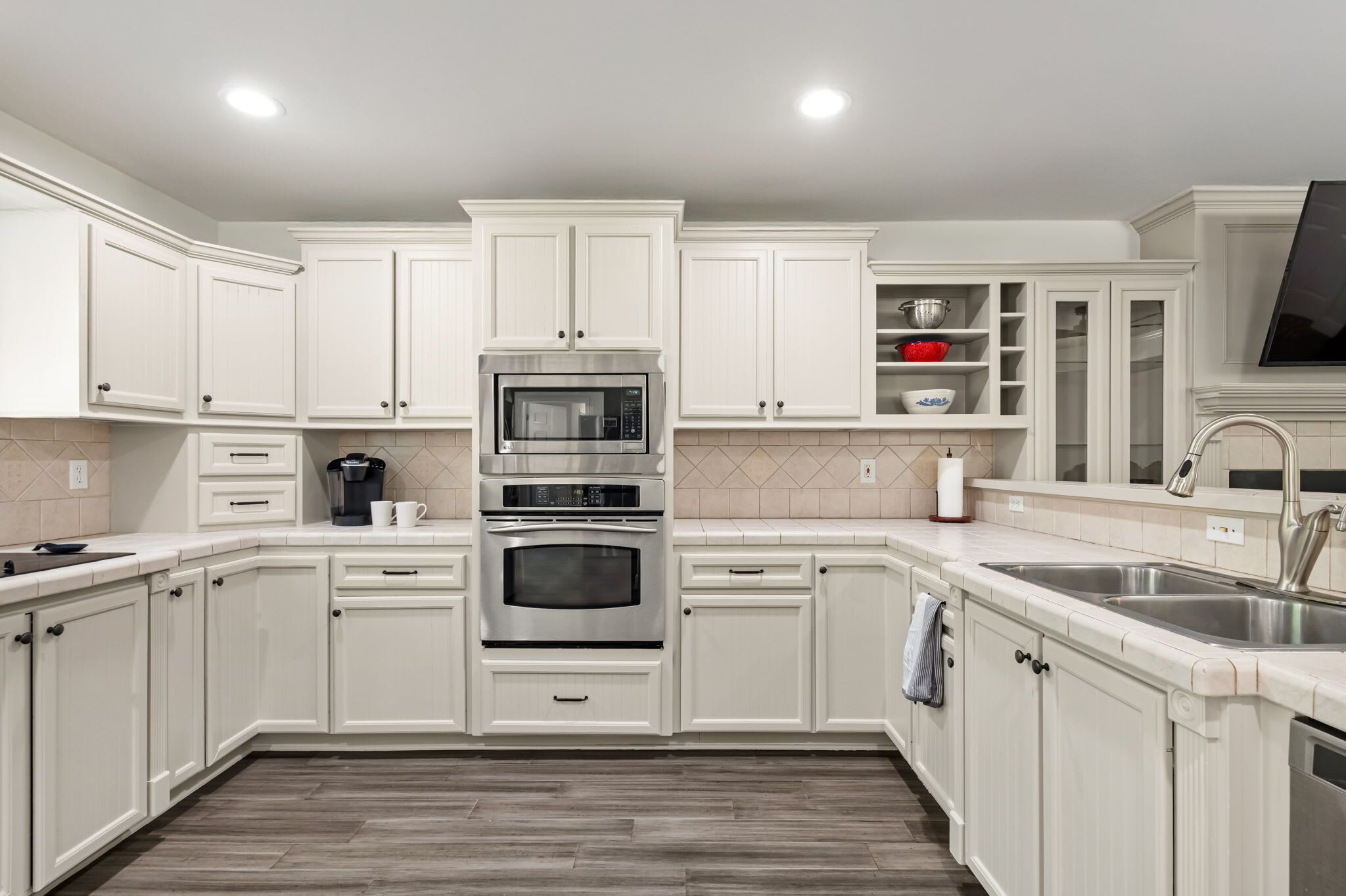 A kitchen with white cabinets, two ovens, a sink, and a tiled backsplash.