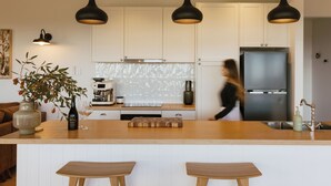Una cocina moderna con armarios blancos, una isla central con taburetes, iluminación colgante y un refrigerador de acero inoxidable.