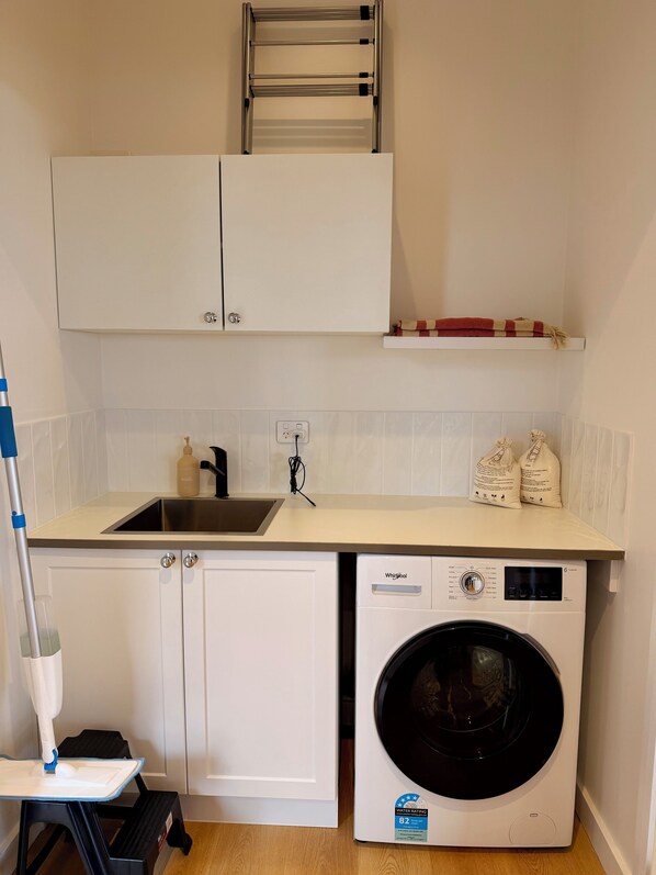 A compact kitchen with a built-in washer and dryer, a sink, cabinets, and a shelf with towels.