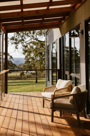 A wooden deck with two wicker chairs, a view of a grassy landscape, and a building with large windows.