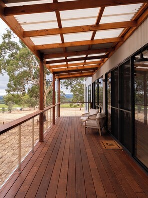 A wooden deck with a pergola, a wicker chair, and a glass door leading to a view of trees and hills.