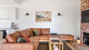 A living room with a brown sofa, a coffee machine, a painting, and a fireplace.