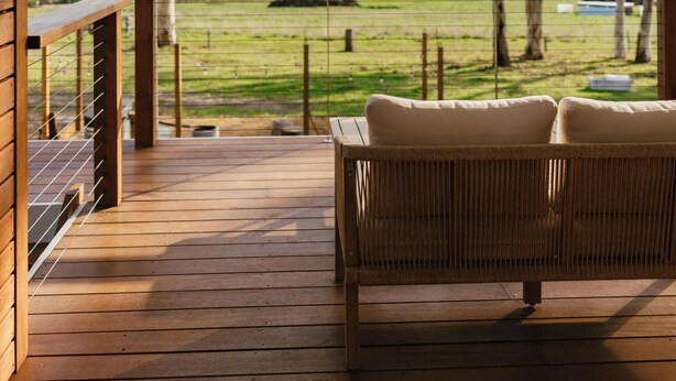 Una terraza de madera con un espacio de descanso techado, con vistas a un paisaje cubierto de césped.