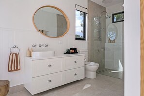A modern bathroom with a white vanity, a round mirror, a toilet, and a glass-enclosed shower.