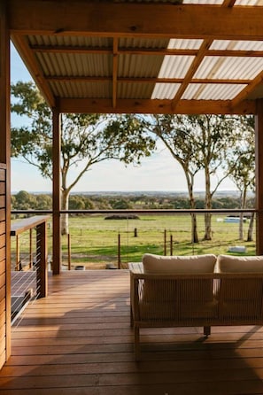 A wooden deck with a view of a grassy field and trees.