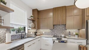 Une cuisine moderne avec des meubles en bois, un dosseret en granit, un évier en acier inoxydable et un four encastré.