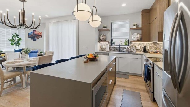 Une cuisine moderne dotée d’un îlot central, d’appareils électroménagers en acier inoxydable et de luminaires suspendus.