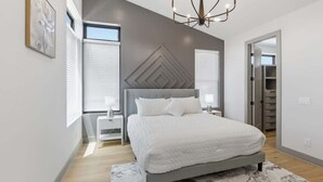 Une chambre moderne avec un grand lit, un lustre et un motif géométrique sur le mur.