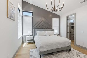 Ein modernes Schlafzimmer mit einem großen Bett, einer Chandelierleuchtre und einem geometrischen Wanddesign.
