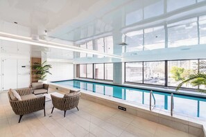 Ein moderner Poolbereich im Innenbereich mit Glasdach, Liegemöglichkeiten am Pool und Blick auf die Stadt.