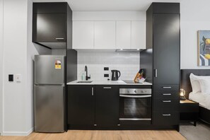 Eine kleine Küche mit Kühlschrank, Herd und Spüle, neben einem Bett mit Nachttisch.