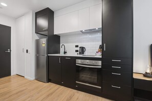 A modern kitchen with black cabinets, a stainless steel refrigerator, a built-in oven, and a white tiled backsplash. - CBD Retreat Studio Nearby Skytower Pool Gym Sauna (Auckland CBD)