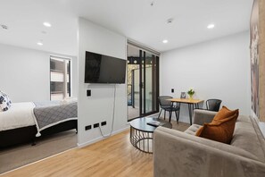 A modern living room with a bed, sofa, TV, and a dining area with chairs and a table. - CBD Retreat Studio Nearby Skytower Pool Gym Sauna (Auckland CBD)