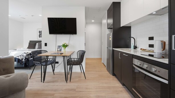 A modern kitchen with a dining area, a flat-screen TV, and a small table with chairs. - CBD Oasis Studio Pool Sauna & Gym Near Skytower (Auckland CBD)