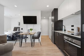 A modern kitchen with a dining area, a flat-screen TV, and a small table with chairs. - CBD Oasis Studio Pool Sauna & Gym Near Skytower (Auckland CBD)