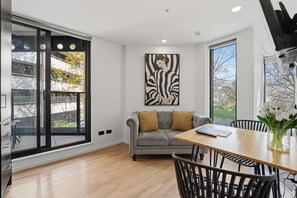 A modern living room with a sofa, a dining table, and a large window. - CBD Oasis Studio Pool Sauna & Gym Near Skytower (Auckland CBD)