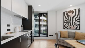 A modern kitchen with a large window, a dining area with a table, and a sofa. - CBD Oasis Studio Pool Sauna & Gym Near Skytower (Auckland CBD)