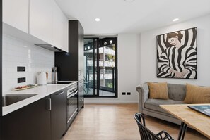 A modern kitchen with a large window, a dining area with a table, and a sofa. - CBD Oasis Studio Pool Sauna & Gym Near Skytower (Auckland CBD)