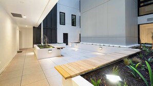 A modern outdoor area with a wooden deck, white planters with plants, and a tiled floor. - CBD Oasis Studio Pool Sauna & Gym Near Skytower (Auckland CBD)