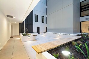 A modern outdoor area with a wooden deck, white planters with plants, and a tiled floor. - CBD Oasis Studio Pool Sauna & Gym Near Skytower (Auckland CBD)