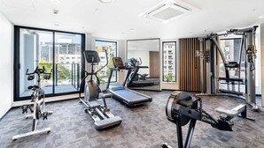 A modern gym with cardio machines, a mirror, and large windows offering city views. - CBD Oasis Studio Pool Sauna & Gym Near Skytower (Auckland CBD)