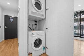 A laundry room with a front-loading washer and dryer, a control panel, and a door with a sign. - CBD Oasis Studio Pool Sauna & Gym Near Skytower (Auckland CBD)