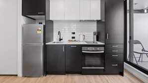 A modern kitchen with a refrigerator, oven, and black cabinets. - CBD Oasis Studio Pool Sauna & Gym Near Skytower (Auckland CBD)