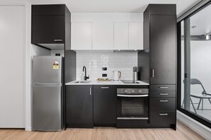 A modern kitchen with a refrigerator, oven, and black cabinets. - CBD Oasis Studio Pool Sauna & Gym Near Skytower (Auckland CBD)
