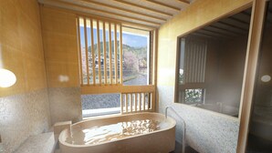 Ein modernes Badezimmer mit einer freistehenden Badewanne, einem Fenster mit Blick auf eine gebirgige Landschaft und einer Wandverkleidung aus Holzlamellen.