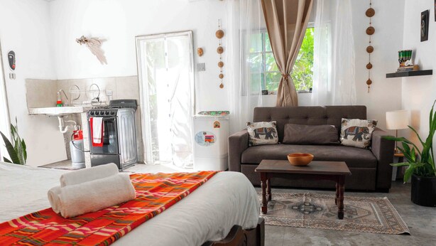 A bedroom with a bed, a sofa, a small table, and a window with curtains.