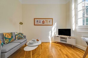 Un salon moderne avec un canapé gris, une table basse, un téléviseur à écran plat et une œuvre d’art encadrée accrochée au mur.