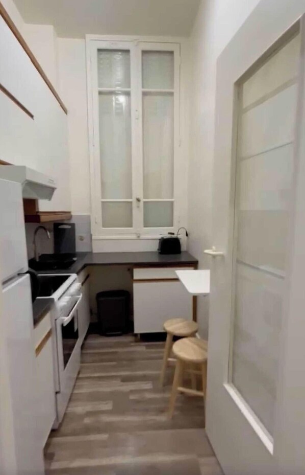Une cuisine de taille réduite avec des meubles blancs, une fenêtre, un évier et un petit tabouret.