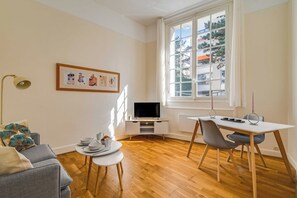 Un salon moderne doté d’un téléviseur à écran plat, d’une table à manger avec des chaises, d’un canapé, d’une petite table d’appoint et d’une fenêtre offrant une vue sur les bâtiments.