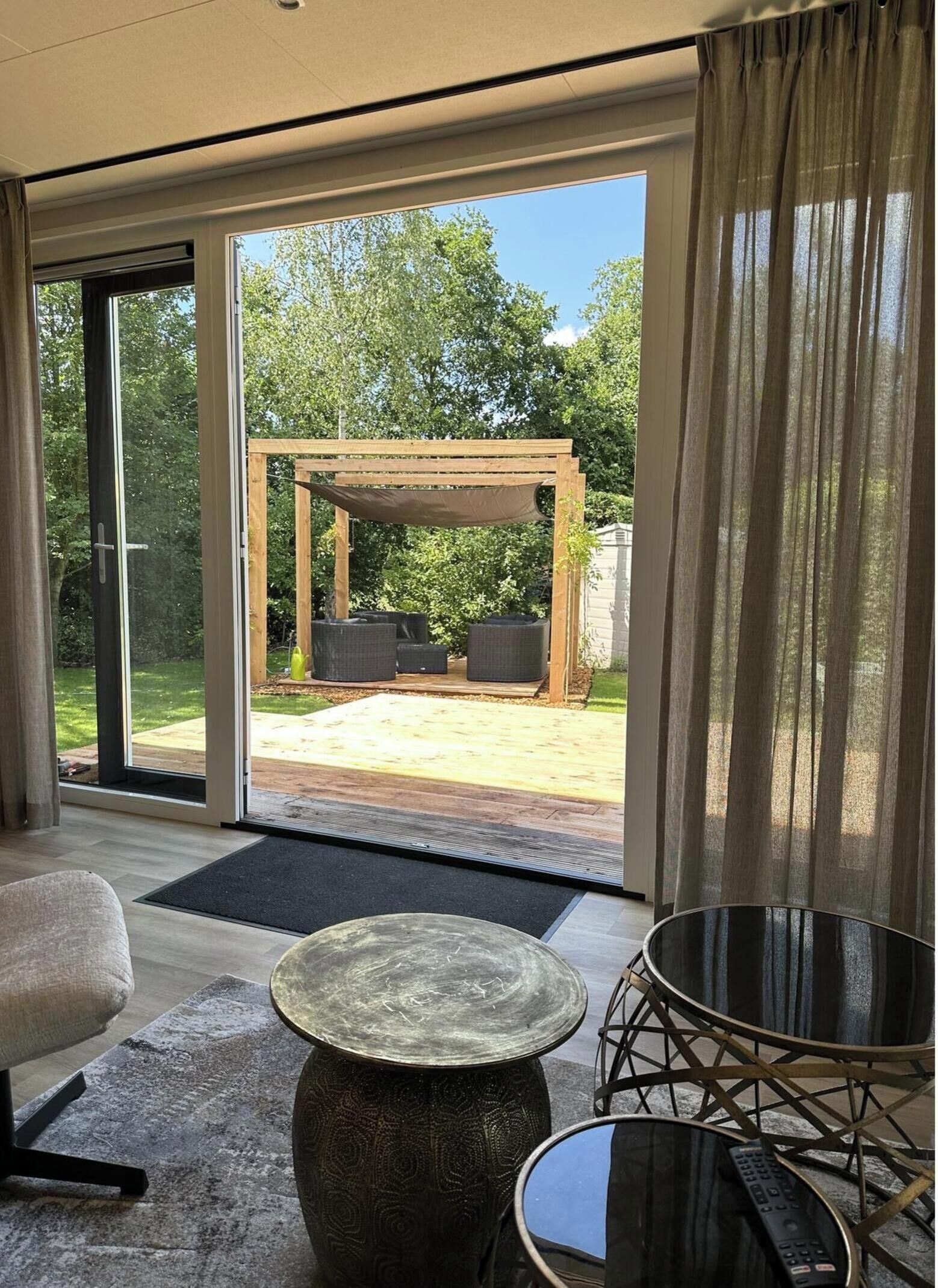 A modern room with a sliding glass door leading to an outdoor patio, a round table, a chair, and a pergola structure.