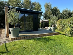 A modern outdoor patio with a glass enclosure, potted plants, and a wooden deck. - Chalet de Blauwe Regen With Sun Terrace (Balkbrug)