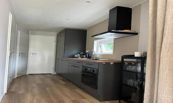 A compact kitchen with dark cabinetry, a window, and a built-in oven. - Chalet de Blauwe Regen With Sun Terrace (Balkbrug)