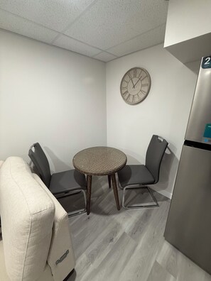 A small room with a round table, two chairs, a clock, and a refrigerator.
