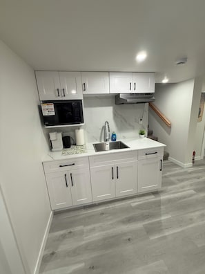 A modern kitchen with white cabinets, a stainless steel sink, a microwave, and a built-in oven.