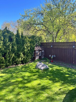 A backyard with a wooden fence, a large rock, and a small shed.