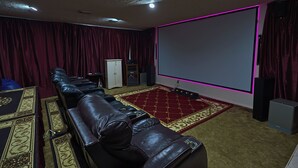 A home theater room with a large screen, leather recliner seating, a carpeted floor, and a speaker. - Willow Tree House - Private Cinema (Houston)
