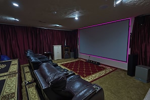 Ein Heimkino mit großer Leinwand, Ledersesseln, Teppichboden und Lautsprecher.