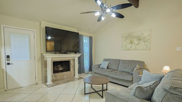 A living room with a fireplace, a sofa, a coffee table, and a ceiling fan. - Willow Tree House - Private Cinema (Houston)