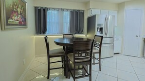 A dining area with a table and chairs, a refrigerator, and a window with curtains. - Willow Tree House - Private Cinema (Houston)