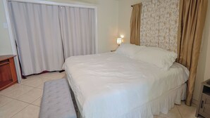 A bedroom with a bed, a bench, a nightstand, a lamp, and curtains. - Willow Tree House - Private Cinema (Houston)