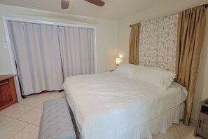 Ein Schlafzimmer mit Bett, einer Bank, einem Nachttisch, einer Lampe und Vorhängen.